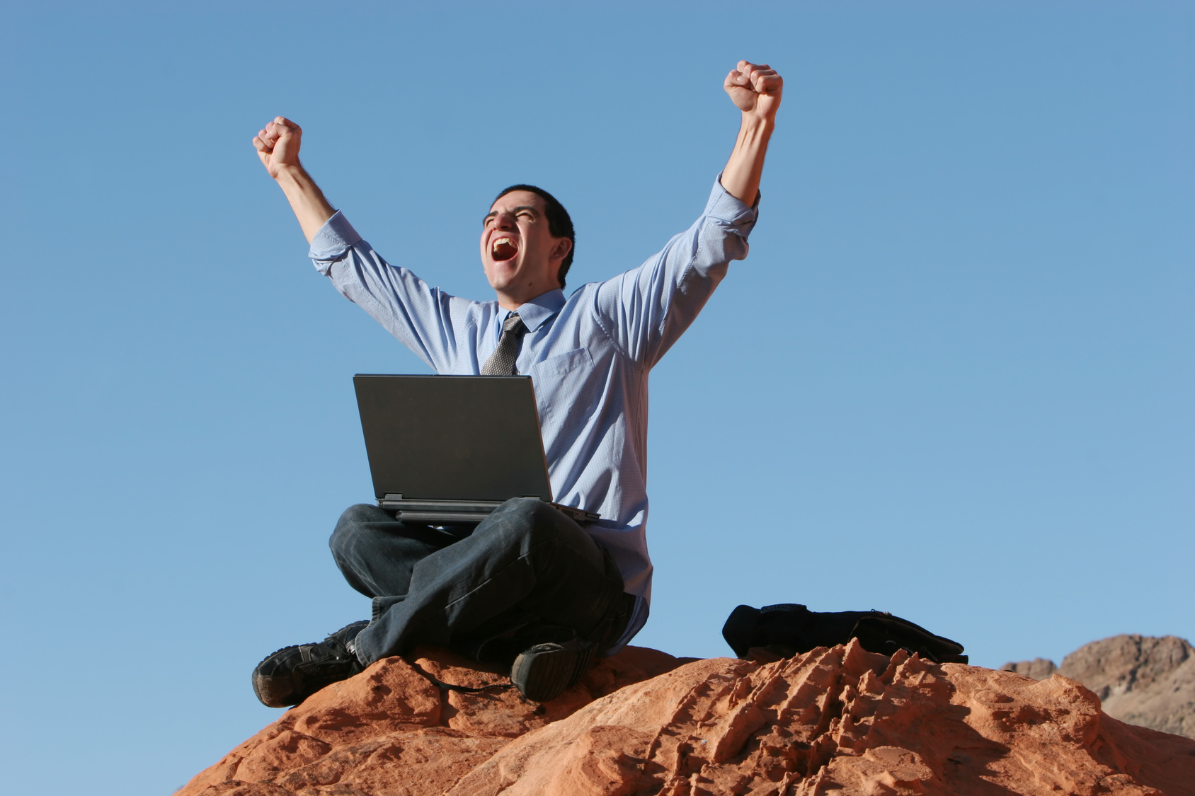 Happy businessman working on laptop on top of the hill